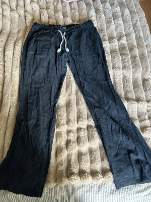 Svarta linnebyxor från Roxy  - Snygga svarta linnebyxor med avslappnad passform och breda ben. Byxorna har resår i midjan och vit dragsko samt fickor fram och bak. Perfekta för en chill och stilren look. Tillverkade i lätt och luftigt linnematerial.