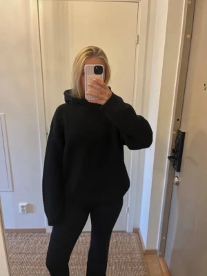 Svart stickad hoodie - En enkel och stilren svart stickad hoodie med huva. Hoodien har en avslappnad passform och långa ärmar. Perfekt för dig som gillar en clean och bekväm look. Materialet är mjukt och lite tjockare, vilket gör den extra mysig.