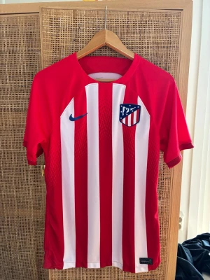 Atlético Madrid matchtröja Stl S - Snygg matchtröja från Atlético Madrid med klubbmärke på bröstet och blå Nike-logga. Tröjan har korta ärmar, rund hals och är tillverkad i ett lätt, ventilerande material som passar perfekt till fotbollsträning eller match.