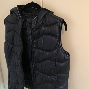 Väst - En trendig och lättstylad väst i mörkblått samt med en luva. Varsamt använd så den är i toppskick!