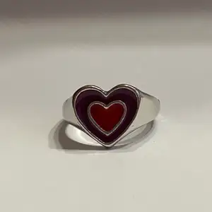 Silverring i form av röd-rosa hjärta.