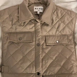 Mörkbeige väst na-kd - Helt oanvänd, lappen kvar. Croppad ganska bred quiltad väst. Går att spänna  åt (bild 2) storlek 36 men skulle säga att den passar mellan xs-m💕