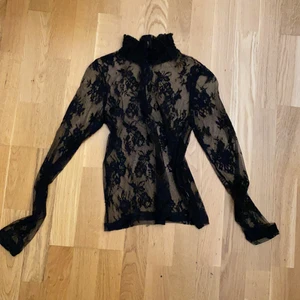 Svart blus, Storlek XS - En tunn svart blus som är synlig (man kan välja att ha något under eller inte. Har blommiga mönster på både fram och baksidan av tröjan. Tajt krage men tjockare vid kragen än resten av blusen. 9 knappar på baksidan av blusen. Köpt i bikbok i storlek XS. Aldrig använd.
