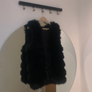 Svart fejk päls väst - Nyköpt pälsväst i storlek S-M. Sitter väldigt bra på, pälsen ramlar ej av. Kort och kommer ner till midjan.