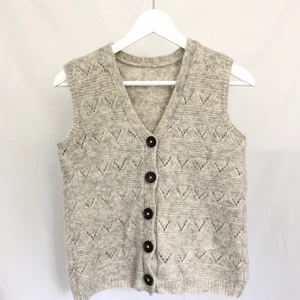 Stickad väst med knappar - Säljer denna stickade väst som jag köpt second hand. Några av knapparna var trasiga vid köpet så alla är utbytta. Färgen är ljus grå/beige. Storlek står inte men skulle säga att det är S. Frakt tillkommer.