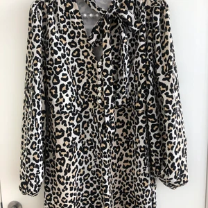 Svensk design märke Brave@, leoprint  - Leoprint klänning, fina ballongärmar, volang längst ner på klänningen, söta knappar framtill, och band som sitter fast i kragen,  knytblus känsla (man kan gömma banden innanför klänningen om man vill). Dragkedja på sidan av klänningen, Lyxig klänning. 