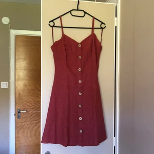 Linneklänning - Härlig terrakottafärgad klänning i linnetyg, lantliga knappar och korsade band i ryggen. Smala justerbara axelband. Klänningen följer figuren upptill för att sedan vara luftig i kjolen 💃🏼 Nyskick!