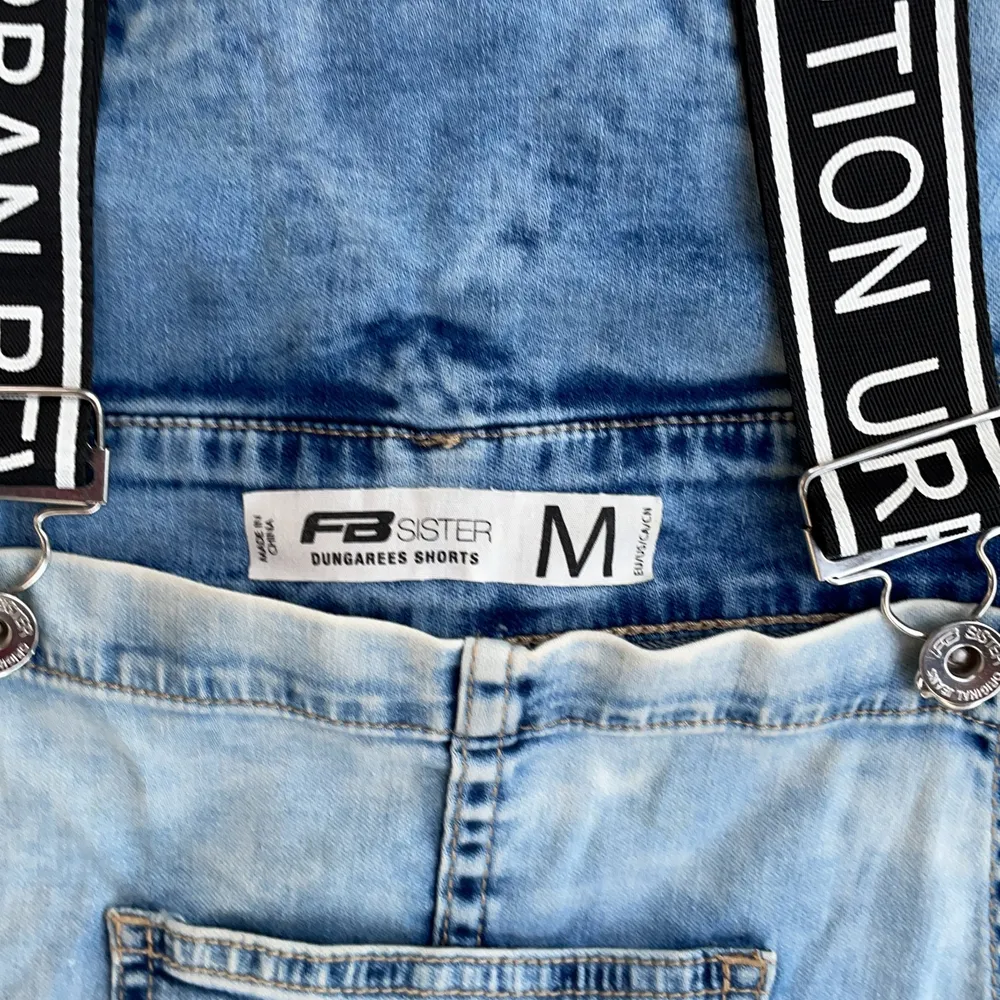 Ljusblå jeans shorts overall från FB sister. Svarta band med vit text på, fickor och silver knappar💕👍🏻. Shorts.