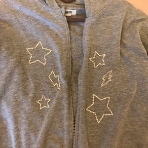 Rhinestones zip-up grå - En jättefin zip-hoodie med rhinestones som jag har satt på själv🥰 stenarna verkar sitta bra men skulle ändå rekommendera handtvätt. Kan skicka med lite extra rhinestones som man kan sätta på själv ifall nån ramlar av💞själva hoodien är i barnstorlek 13-14 men passar mig som är 170 och har xs😊håll gärna utkik då jag kommer lägga upp fler plagg med rhinestones i framtiden💗frakt tillkommer🥰lite inspererad av en annan säljare på Plick som jag har tappat bort namnet på😅