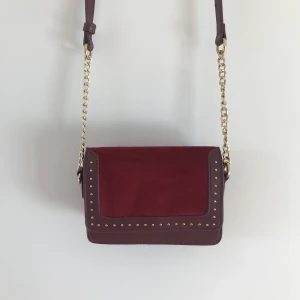 Liten vinröd axelväska - Liten och söt axelväska i vinröd sammet. Säljer då den aldrig kom till användning. Bandet är justerbart. Köparen står för frakt 