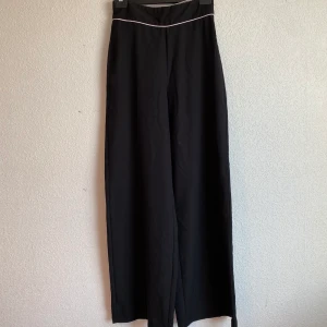 Svarta kostymbyxor  - Svarta kostymbyxor med en vit rand detalj, strl 36