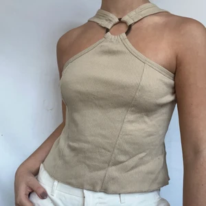 Beige Y2k halterneck - KÖP DIREKT FÖR 210kr! Helt underbar beige halterneck. Perfekt för dig som letar efter kläder från början av  2000-talet! Plagget visas på en S men passar säkert även M. Toppen är i gott skick utan sunflower defekter. Den går att vändas bak och fram beroende på om man vill ha ringen fram eller trycket!  Högsta bud 190kr. Pågår tills annonsen markerats såld så buda på! Du vinner om ingen budar mer än dig på 24h
