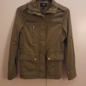 Militär grön jacka strl 34 - Militär grön bomullsjacka från H&M. Längd 60cm, strl 34. Dragsko i midjan. Ej använd.