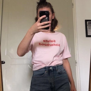 T-shirt - Rosa t-shirt med texten Salute Sisterhod på. Texten är i ett sammetsmaterial