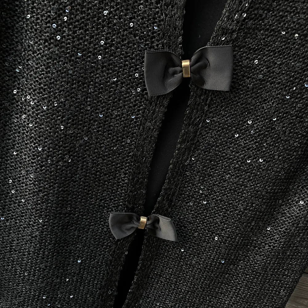Stickad svart tröja med lite paljetter samt rosetter i ryggen. Passar S/M . Tröjor & Koftor.