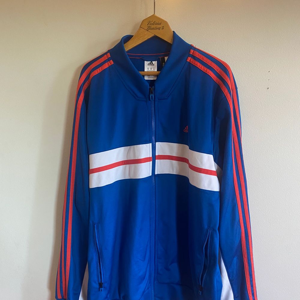 Adidas trackjacket. Köpt på second hand i californien för två år sedan. Ovanlig modell med drapering i vitt fram och oranga ränder längs sidorna . Huvtröjor & Träningströjor.