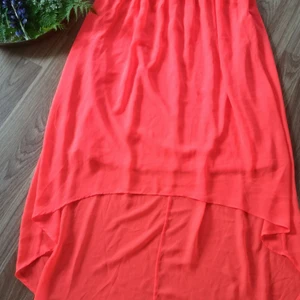 Klänning från Vero Moda  - Klänning med längre parti i bak än i fram. Från Vero Moda. Orange med fina detaljer över bysten och med dragkedja i sidan. Storlek 36