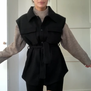 Svart väst med skärp - Ofodrad svart väst i filtmaterial, EJ puffer. Superfin och snygg med en stickad tröja under. Perfekt till hösten och våren!