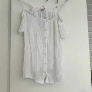 Vit blus med knappar - En vit blus med knappar som går att knäppa upp. Blusen är även of shoulder med justerbara axelband. Toppen är förövrigt ganska stor i storleken så den passar vadå XS och S. Jag har aldrig använt blusen och den är helt som ny.
