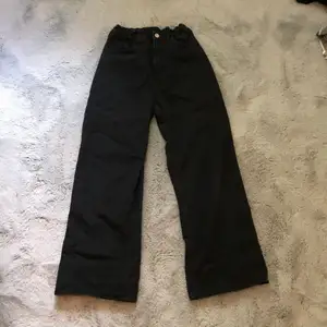 Ett par svarta vida jeans med brons knapp. Fickor både fram och bak, resår i midjan. Använt ganska mycket, men inte överdrivet. Inga tecken på använd.