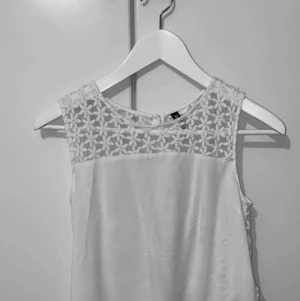 BRODERAD TOPP MED BLOMMOR - Vit topp med broderi (små blommor i broderi), hela ryggen är broderad med knappar. Använd fåtal gånger, mycket bra skick. Strl 34 från H&M (divided by hm)