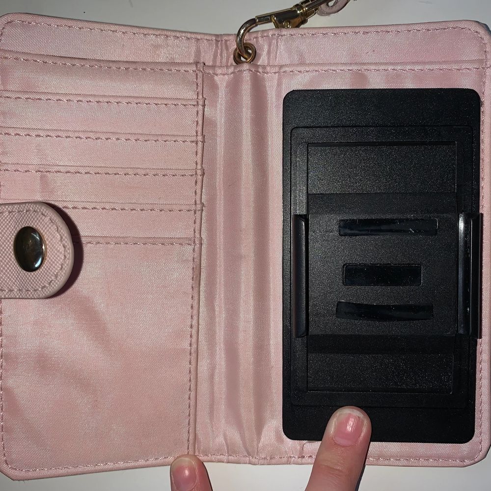 Ett rosa plånboksskal med korthållare i och sedelhållare. Man sätter på mobilen genom att dra i kanterna på svarta delen och sätter på mobilen. När man ska ta bild men bakkamera så trycker man bara upp den svarta delen medans mobilen fortfarande sitter på. Skalet har också ett band som man kan stoppa igenom handen. Skalet är runt 2 år gammalt. . Övrigt.