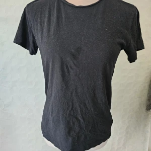 Svart t-shirt från 157 - En svart t-shirt från 157 i storlek XS. T-shirten är tillverkad av 100% bomull och har korta ärmar.