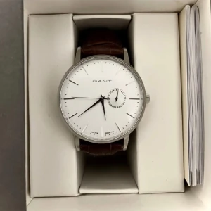 Gant klocka  - Gant klocka med silver detaljer.  Brunt läderband.  Innehar kvittot som förstås medföljer.  Original box.  Batteri behöver bytas, kostar ca 29 :- 