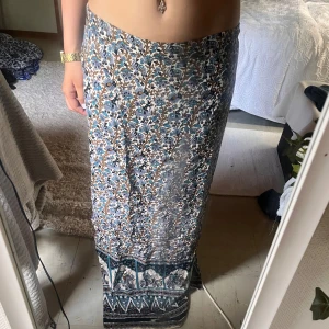 Mönstrad långkjol - En mönstrad långkjol med blommigt mönster i olika nyanser av blått, grönt och beige. Kjolen har en rak passform och är tillverkad i ett lätt och bekvämt material.