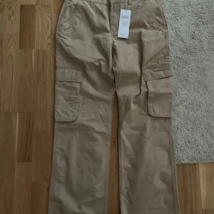 Low waist cargo jeans - Jeansen är helt nya med prislapp! De är inte använda och de har en rak passform med storleken 36. Jag köpte de för 500kr men kommer sälja de för 150kr, priset kan dock diskuteras! Byxorna är i färgen ”mud” (beige) och kan inte hittas i butik. 