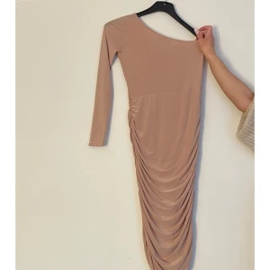 Klänning med axelband  - Klänningen är medellång, materialet är likt satin och i verkligheten har den en babyrosa färg. Klänningen har ”scrunch” på bägge sidorna och detta framhäver kurvorna mer. 