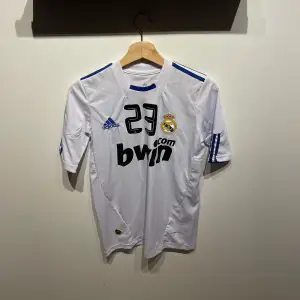 Säljer en replika av Özil Real Madrid tröja från säsongen 2010/11. Storlek: S. Tröjan har använts men är i mycket gott skick. Den klassiska vita designen med klubbens emblem och Özils nummer 23 på ryggen gör den perfekt för samlare eller fans.
