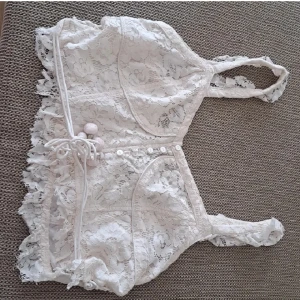 Vit spetskorsett - En elegant vit korsett i spets med detaljer som knytning och knappar. Korsetten har en vacker spetsdesign och är ärmlös med smala axelband.