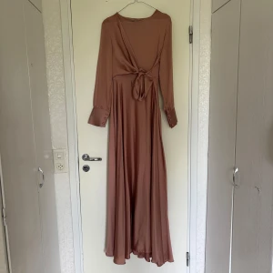 Rosa långklänning från DMN - En elegant rosa långklänning köpt utomlands  med långa ärmar och knytning i midjan. Klänningen är i satin med knappar vid ärmsluten. Storleken är 42 men skulle absolut säga att den passar 38 då jag själv haft den. 