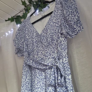 Blommig klänning  - Blå och vit blommig klänning från cubus. Små veck vid bysten och på armarna. Ett snöre runt om för att ge mer form. Det finns en dragkedja på sidan. 