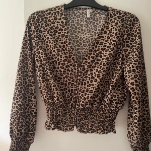 Leopardmönstrad topp från Nelly - En leopardmönstrad topp från Nelly med långa ärmar och v-ringning. Toppen har en ”elastisk” midja och ärmslut, vilket ger en bekväm passform. Storlek M och endast använd ett fåtal gånger. 🐆 ✨🌸