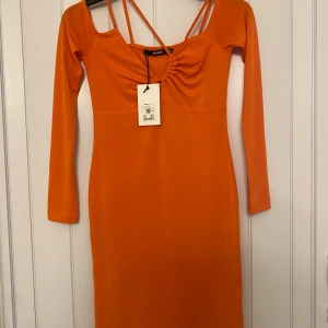 Orang klänning xs - En orange klänning med långa ärmar och axelband. Klänningen har en figursydd passform och en rund halsringning. Den är perfekt för en festlig tillställning eller en kväll ute.