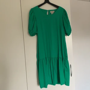 Grön klänning från Residus - En grön klänning från Residus med korta puffärmar och en lös passform. Klänningen har en rund halsringning och en knappdetalj i nacken. använd en gång. 