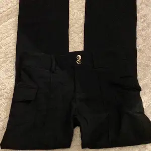 Svarta ”bootcut” byxor i tunnare material (skönare material) från Shein i storlek 32 / XS (S) som har små fickor på sidan och detaljer som två stycken knappar och ett streck i mitten ner till byxorna. 