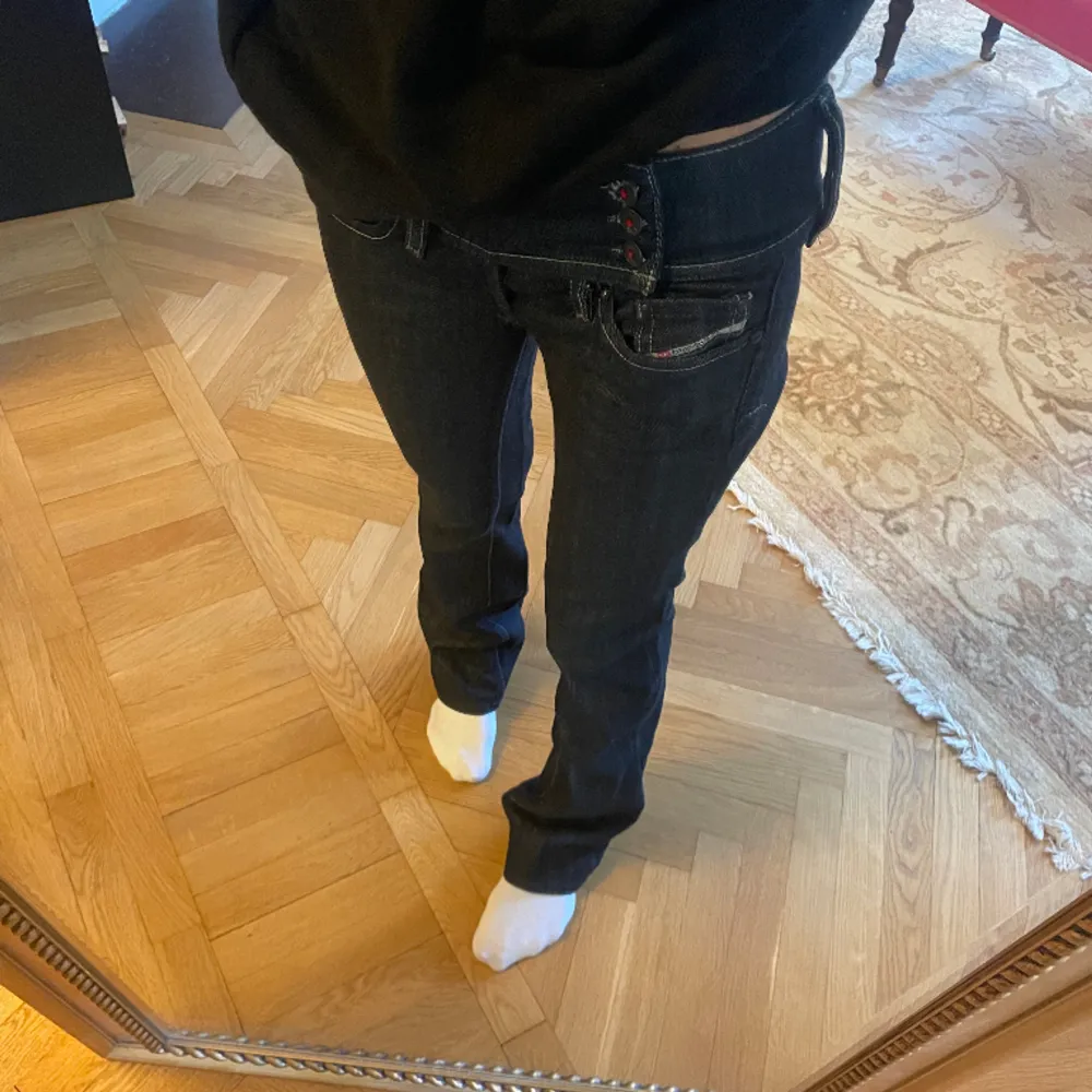 Mörkblå/ svarta lågmidjade jeans från deisel. Jeansen har tre knappar på sidan med röda detaljer på. Passar mellan 34/ 36. Jeans & Byxor.