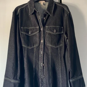 Jeansklänning från H&M - Svart figursydd mini jeansklänning från H&M. Storlek 40. Oanvänd.