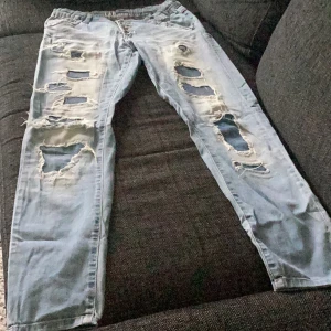 Ljusa slitna jeans - Säljer ett par ljusa jeans med massor av slitningar och hål. De är riktigt coola och har en avslappnad stil. Perfekta för en casual look! De är i bra skick trots slitningarna, som är en del av designen.