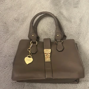 handväska från Lycke - Säljer en handväska från Lycke - Oslo . Väskan är i skinn och har en design med guldiga detaljer. Den har två handtag som är lite slitna och en hjärtformad berlock. Väskan har även ett fack  på baksidan, kontakta mig om intresserad eller om frågor💘