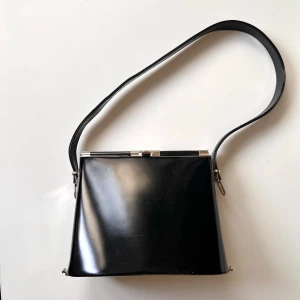 Svart axelväska från Vezzano - Säljer en snygg svart axelväska från Vezzano. Väskan har en stilren design med en metallram och ett lås upptill. Klicka på köp nu <3