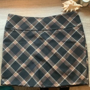 Rutig kjol från H&M Divided - En kort rutig kjol från H&M Divided i färgerna svart, beige och brun. Kjolen har ett klassiskt rutmönster och är i storlek XXS.