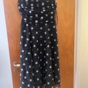 Svart prickig klänning från Jessica Howard - Säljer en superfin vintage svart klänning med vita prickar från Jessica Howard. Klänningen är ärmlös och har smala axelband. Den är perfekt för festliga tillfällen och har en elegant passform. Klänningen är i nyskick och kommer från Beyond Retro. Passa på att fynda denna snygga klänning! 💃