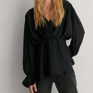 Svart blus med v-ringning - Säljer en elegant svart blus med v-ringning och långa ärmar. Blusen har en lös passform och är perfekt för både vardag och fest. Den är tillverkad i ett mjukt och bekvämt material som känns skönt mot huden. Ärmarna har fina detaljer med knytning vid ärmsluten.