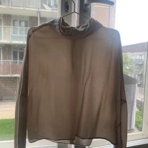 Beige blus från Stockh LM - En elegant beige blus från Stockh LM. Blusen har långa ärmar och en hög krage. Materialet är lätt och genomskinligt, vilket ger ett luftigt och stilrent intryck.