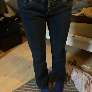 Mörkblå jeansbyxor från Jasper Conran - Ett par mörkblå jeansbyxor från Jasper Conran med broderade detaljer på bakfickorna. Byxorna har en klassisk femficksdesign och är i storlek 38. 