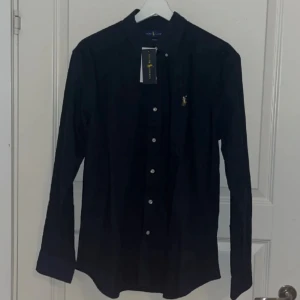 Ralph Lauren Skjorta - Helt ny Ralph Lauren skjorta, skick 10/10. Storlek L passar M. Skön och lätt att styla upp och ner. Marinblå med vita knappar